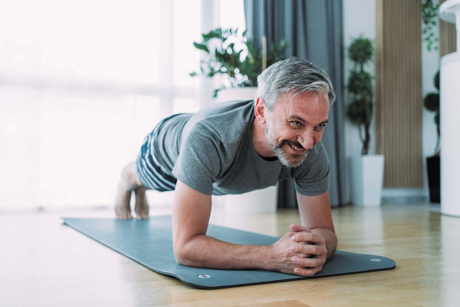 A mature man performs a plank exercise on a mat in his home.