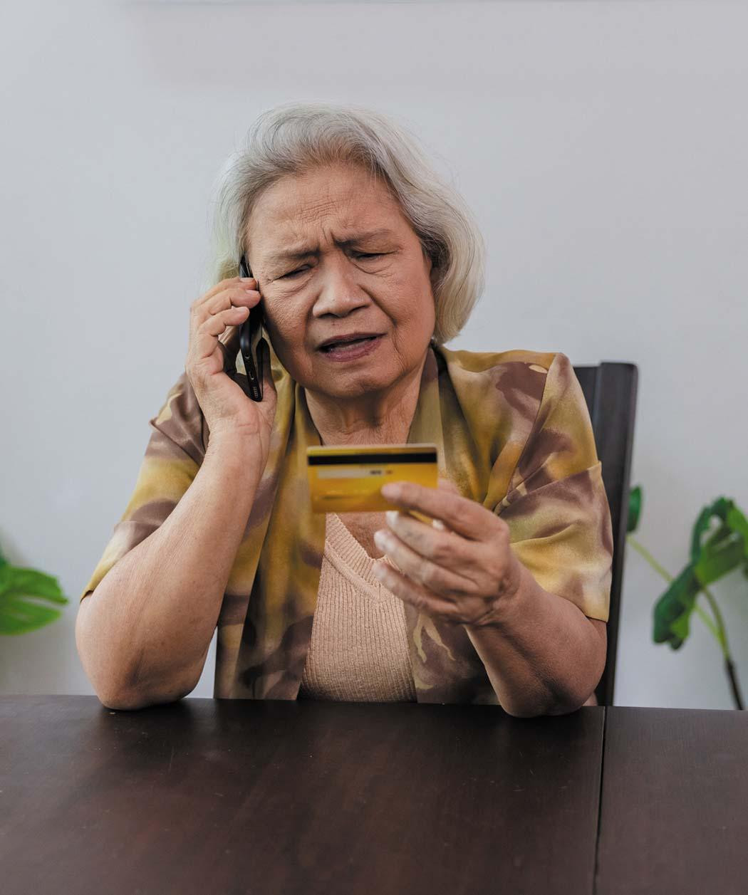 A woman looking concerned while talking on the phone and holding a credit card in front of her.