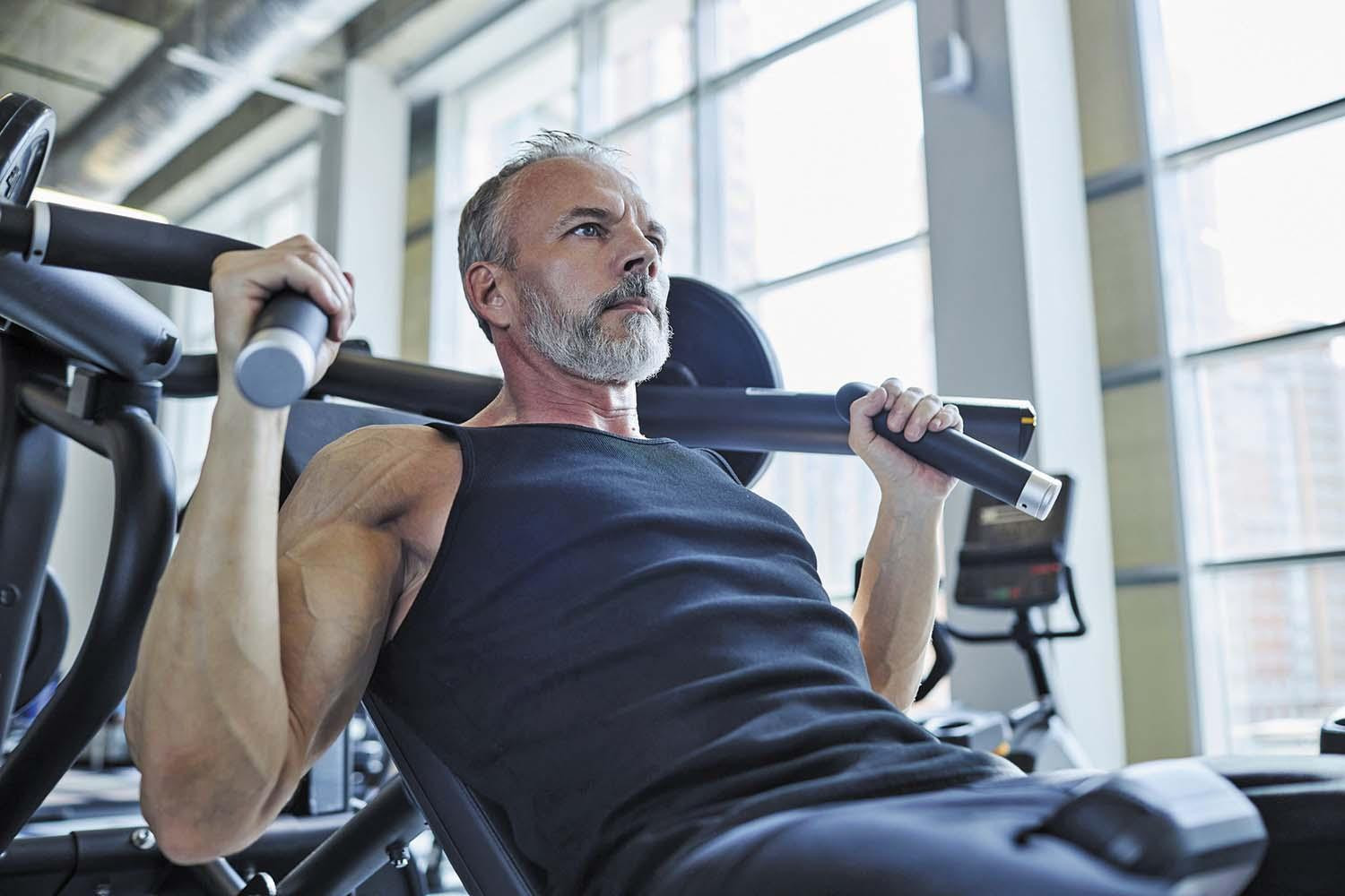 A mature man exercises using a weight machine in a gym.
