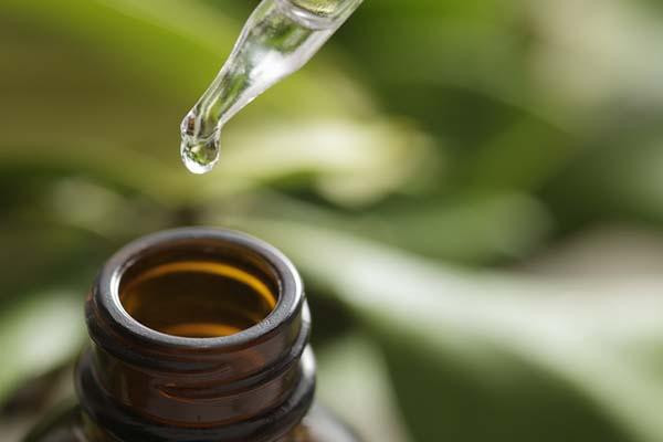 Close-up of the neck of a brown glass bottle and a dropper held above it with a drop of oil hanging off of it.